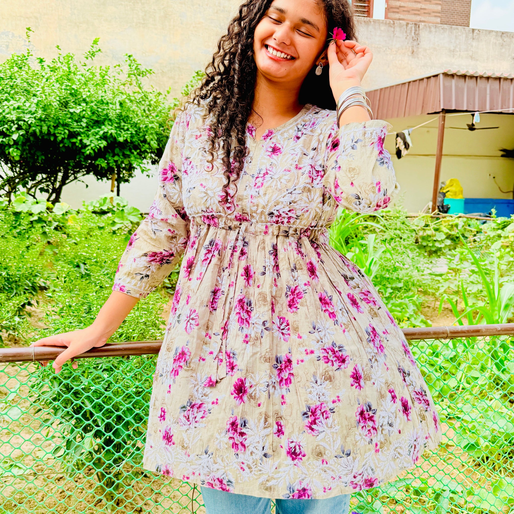 Woman in a floral dress standing outdoors with greenery in the background