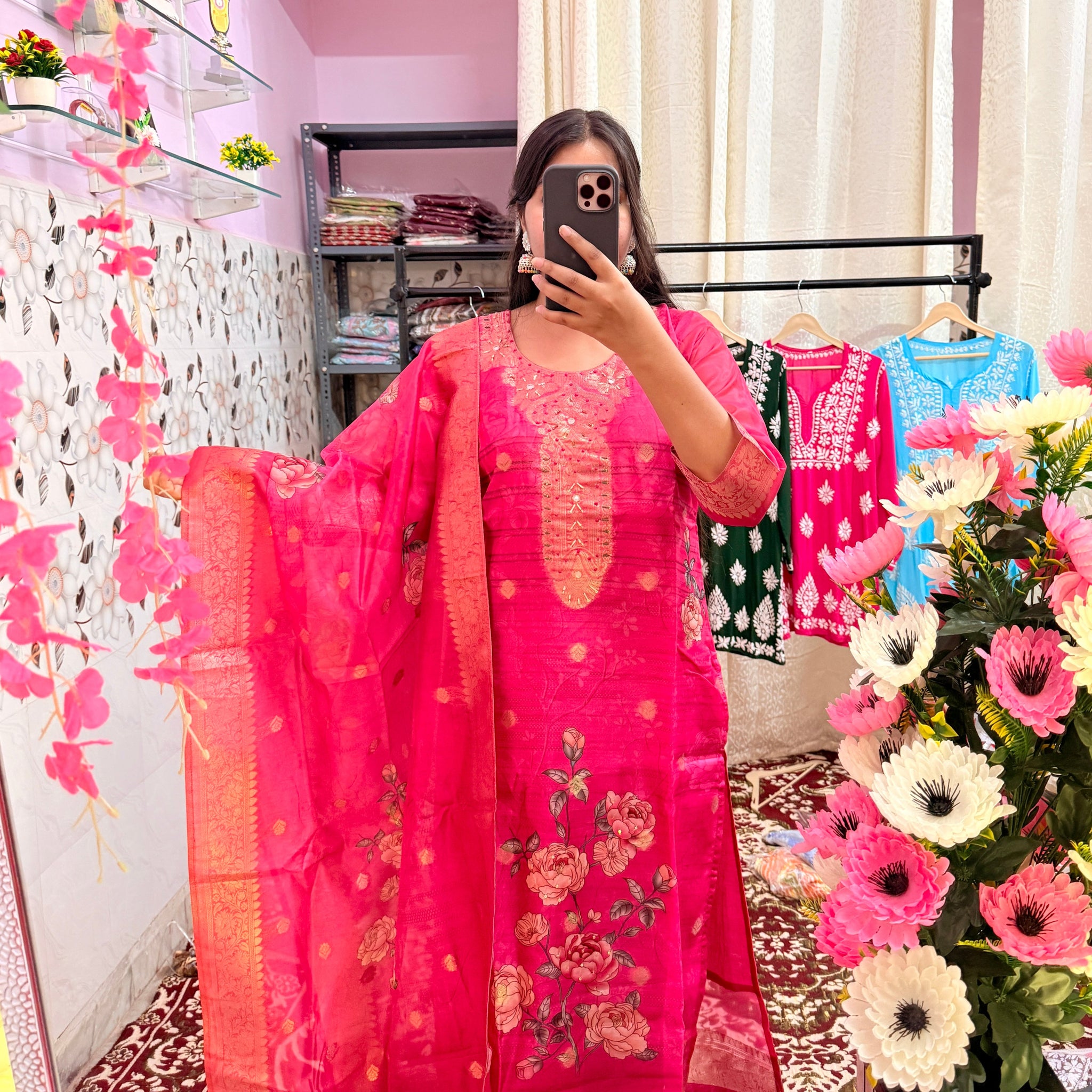 Person wearing a pink traditional outfit with floral patterns in a decorated room.