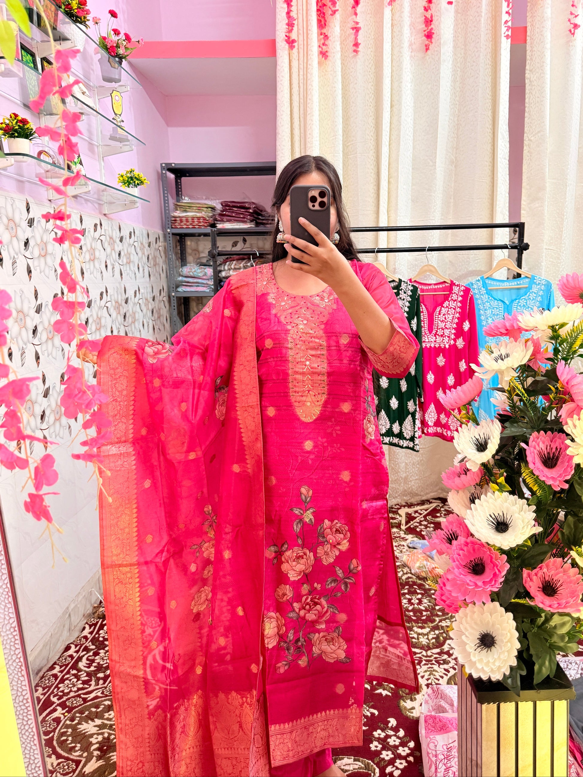 Person wearing a pink traditional outfit with floral patterns in a decorated room.