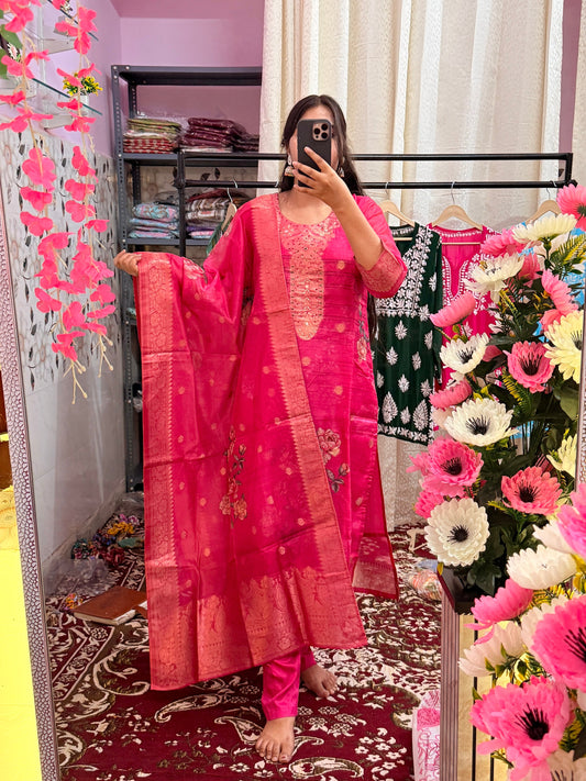 Person wearing a pink traditional outfit standing in a decorated room with flowers and colorful drapes.